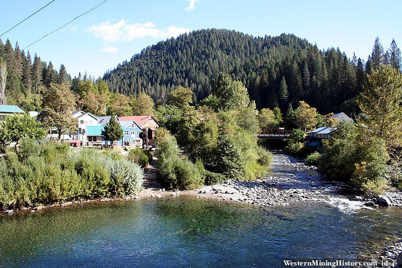 Downieville town with colorful houses, a forested mountain backdrop, and a clear river flowing through the valley.