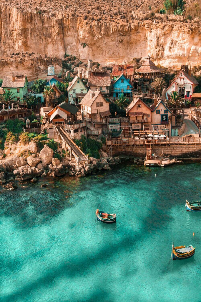 Colorful cliffside village at Popeye Village Malta with turquoise water and boats