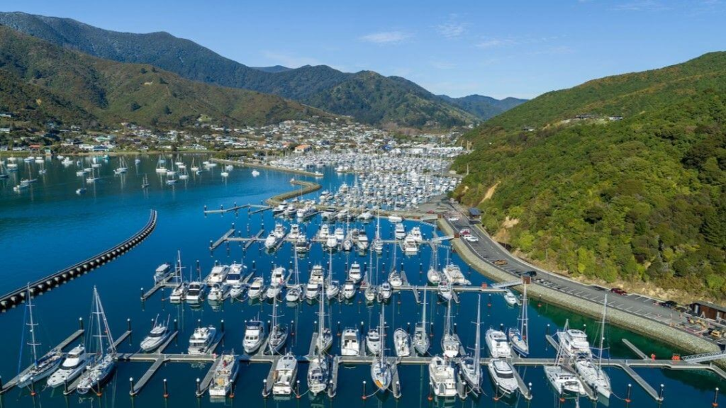 Marina filled with boats and yachts surrounded by green hills and coastal town views.