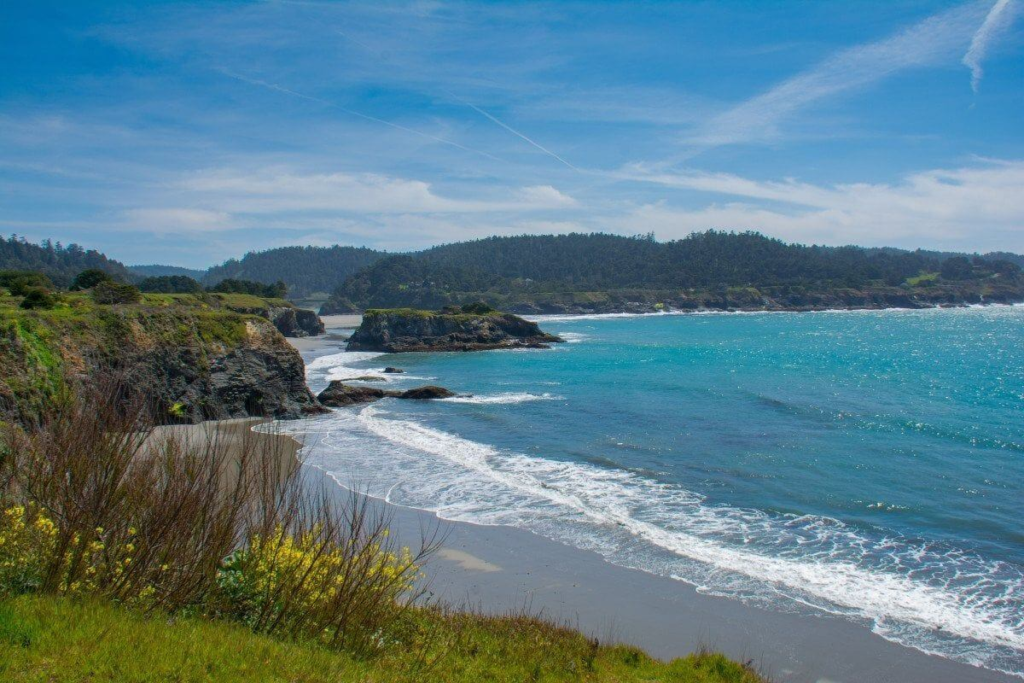 Mendocino County coastline with rocky cliffs, turquoise ocean waves, and a clear blue sky.