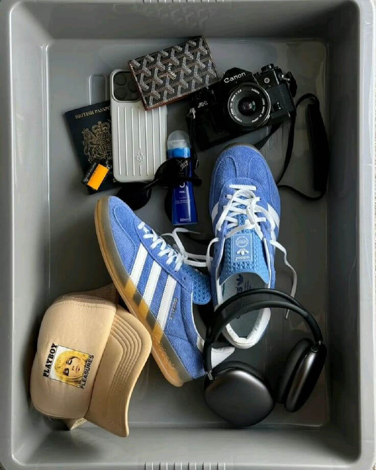 Travel essentials including shoes, camera, passport, headphones, and accessories in a security tray