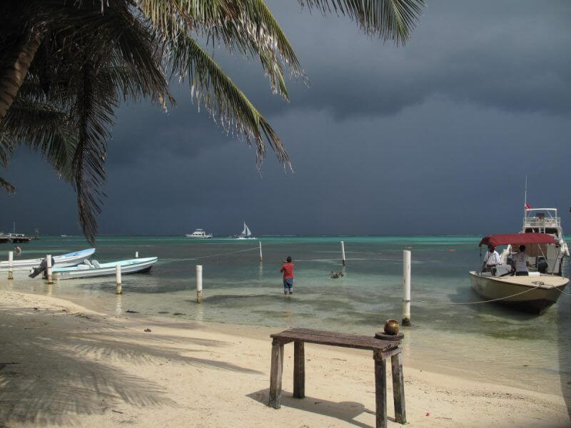Beach in Belize with dark storm clouds and a fisherman in the water