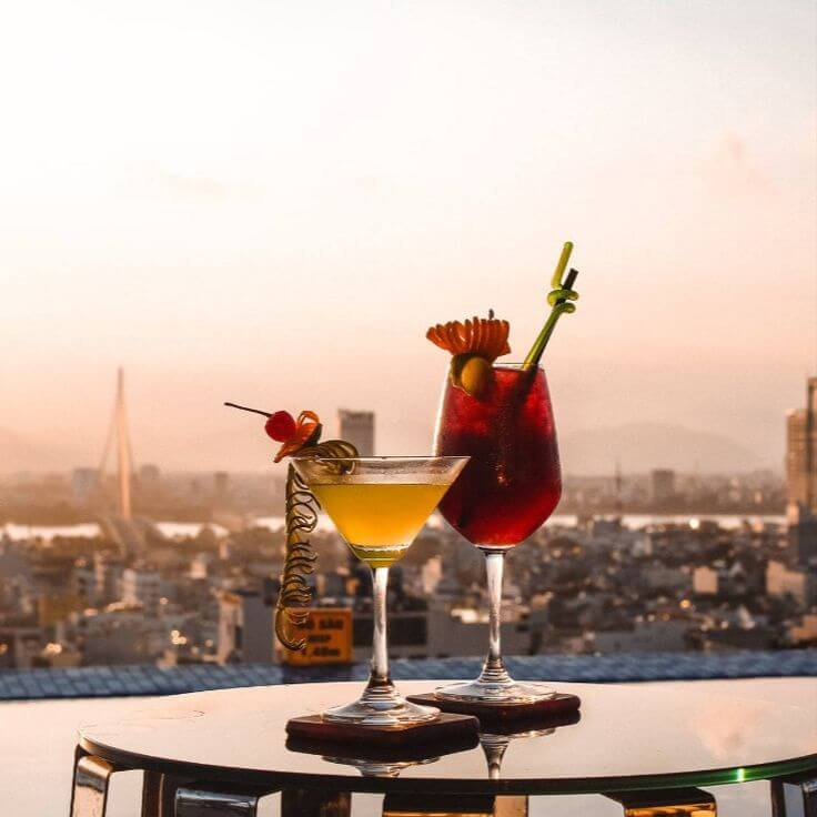 Colorful cocktails on a rooftop bar table overlooking a city skyline at sunset.
