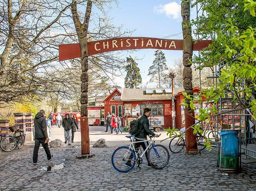 Entrance to Christiania, the free-spirited neighborhood in Copenhagen, with visitors walking and biking under the iconic sign