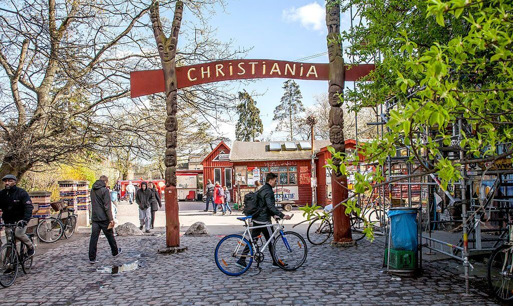 “Entrance to Freetown Christiania in Copenhagen with people walking and cycling.”