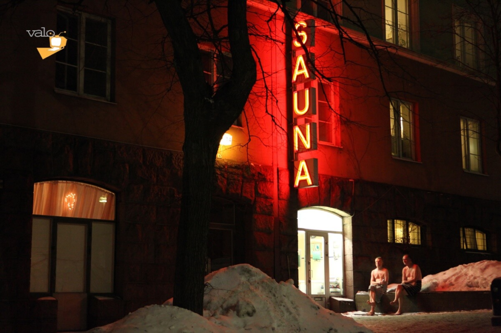 Traditional Finnish sauna building with glowing red sign on a snowy Helsinki street at night