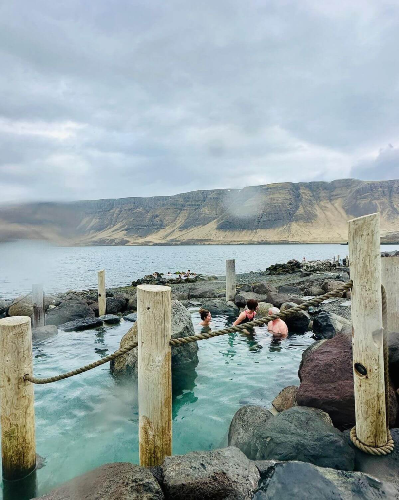 People relaxing in natural hot springs by the sea near Reykjavík, Iceland with mountain views.