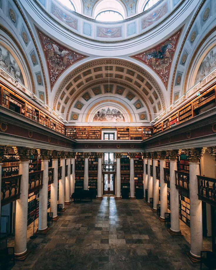 Grand historic library interior in Helsinki, Finland with domed ceiling and classical architecture.