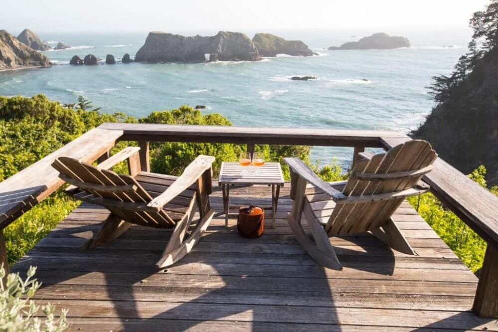 Wooden deck with lounge chairs overlooking a rugged coastline and blue ocean at Harbor House Inn.