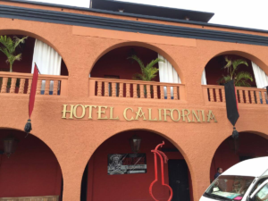 Front view of the orange-painted Hotel California building with arches, balconies, and palm plants.