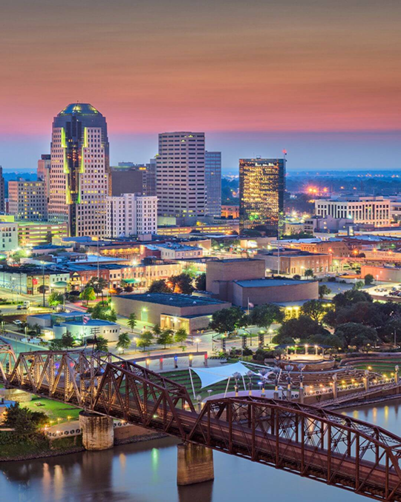 Aerial view of Shreveport, Louisiana, with a river bridge and city skyline at sunset.