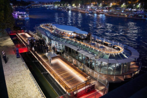 Night view of a luxury river cruise boat docked along the waterfront, illuminated with lights.