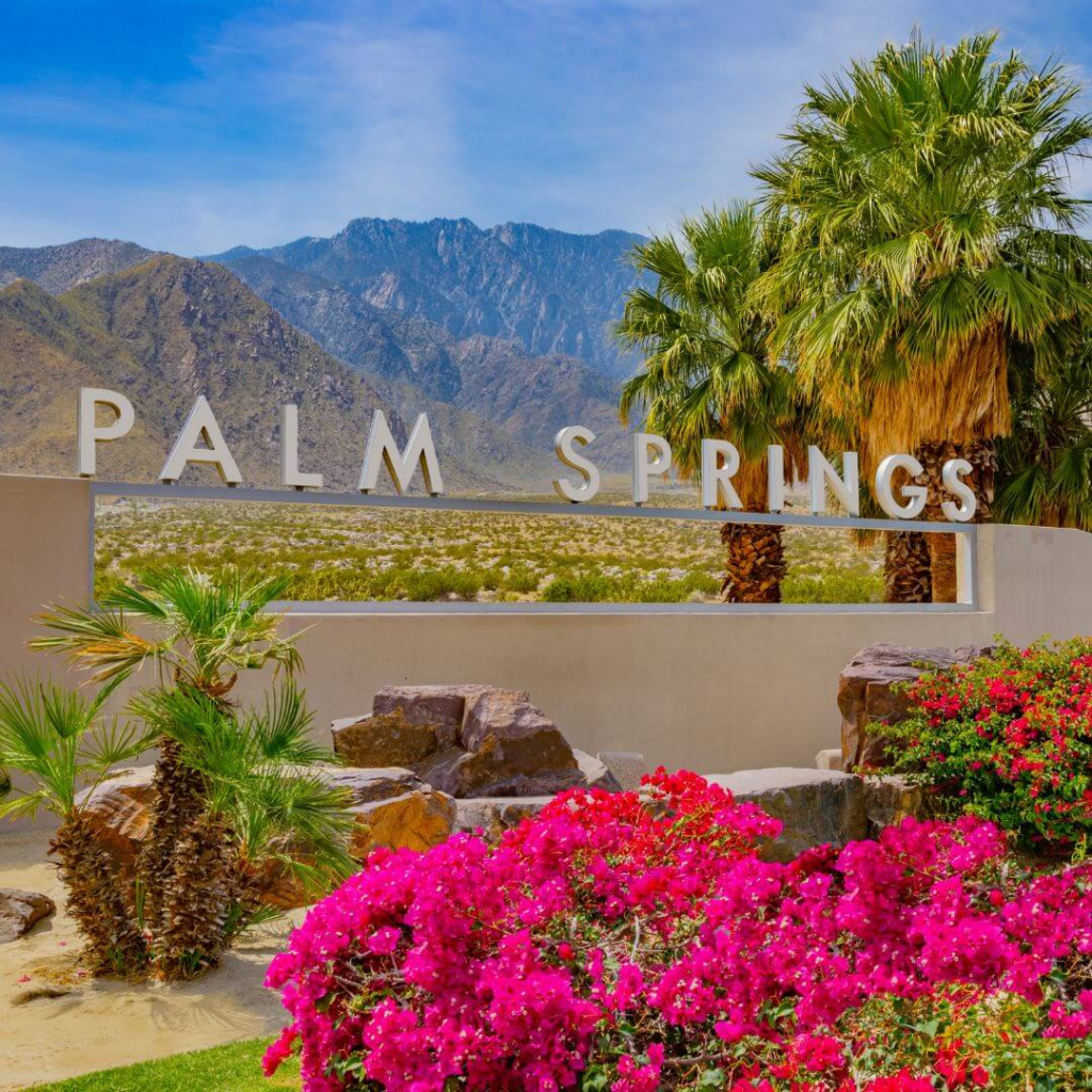 Palm Springs sign with vibrant pink flowers and desert mountains in the background.