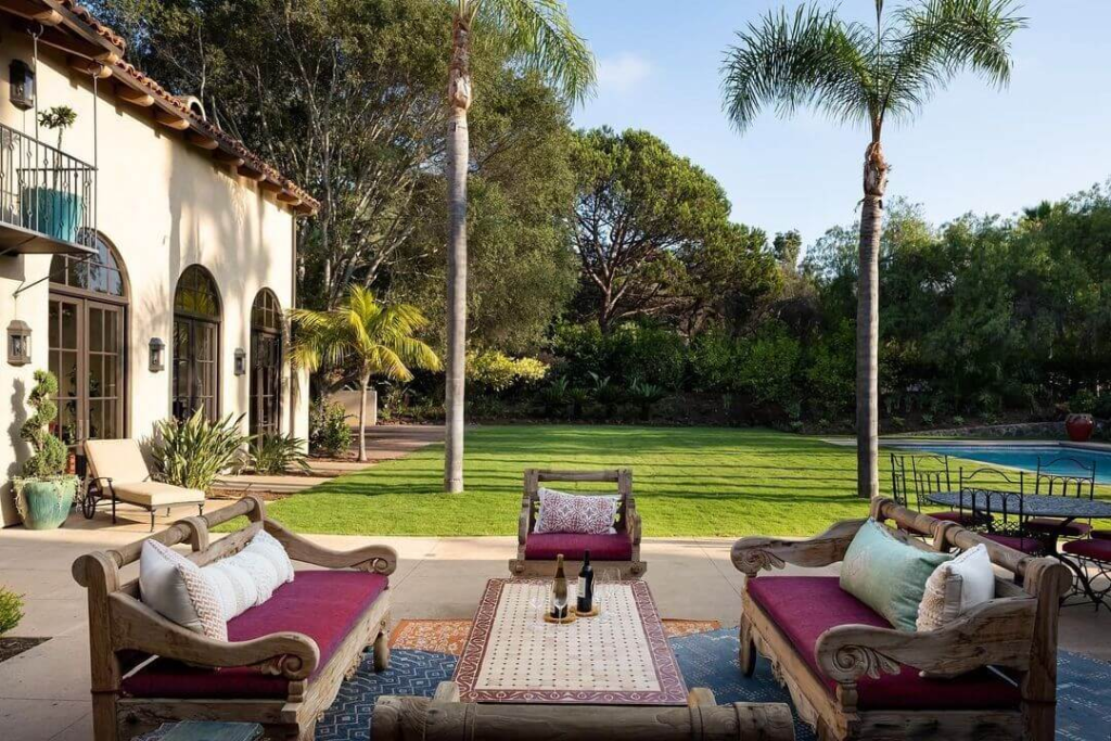 Luxurious outdoor patio at Rancho Valencia Resort with wooden sofas, palm trees, lush lawn, and a poolside view