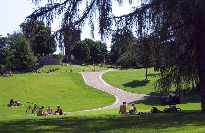 People relaxing on the grass at a sunny park in Helsinki with a winding path.