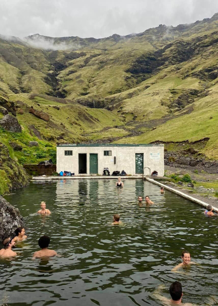People relaxing in a natural hot spring pool surrounded by green mountains in Iceland