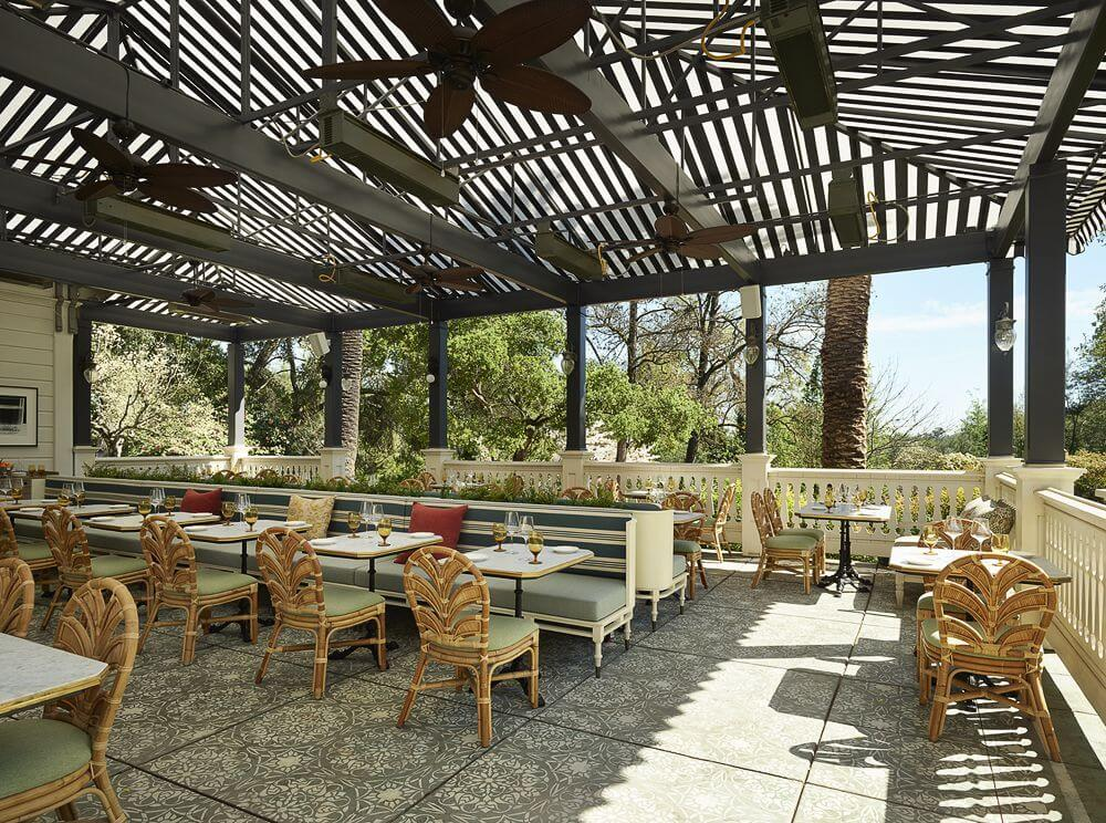 Stylish outdoor dining patio at The Madrona with patterned tiles, rattan chairs, ceiling fans, and garden views.