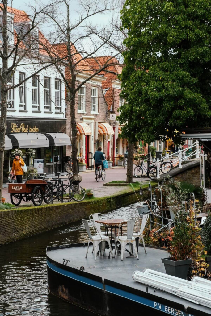 Canal-side view of a charming Dutch street with bicycles, outdoor seating, and shops in the background.