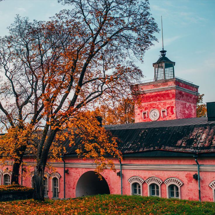 Suomenlinna’s pink clock tower surrounded by autumn trees in Helsinki.