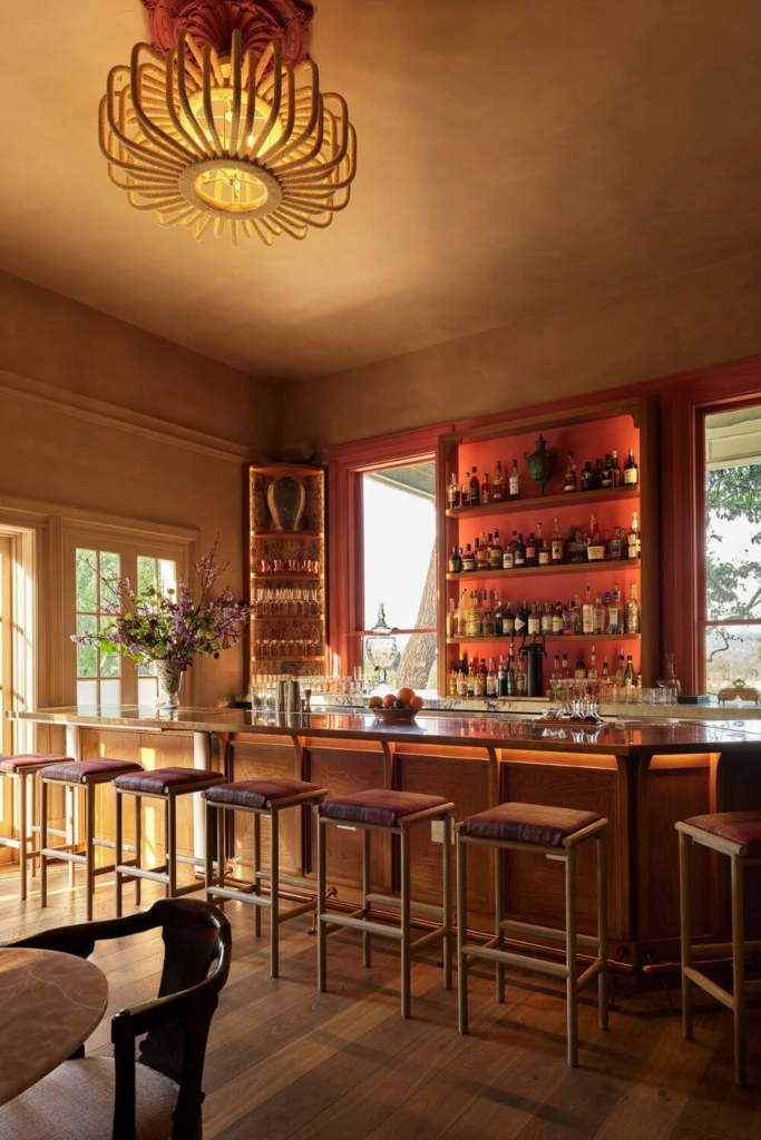 Warm, elegant bar interior with wooden stools, soft lighting, and shelves filled with bottles behind a marble countertop