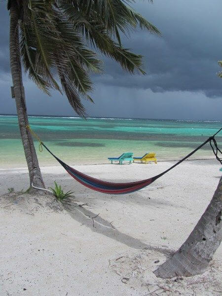 Beach in Belize with hammock, storm clouds, and colorful chairs 
