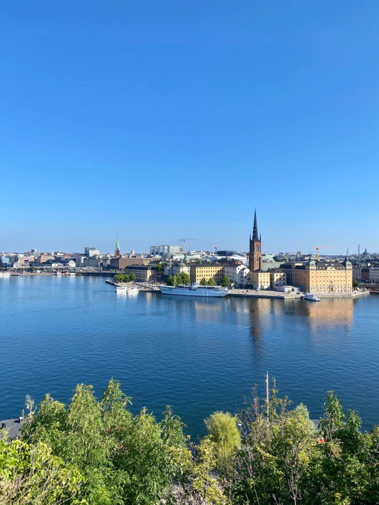 "View of Stockholm's skyline from Monteliusvägen with church spire and clear blue sky.