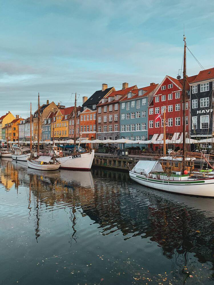 Colorful waterfront buildings and docked boats reflecting on the calm canal at Nyhavn in Copenhagen.