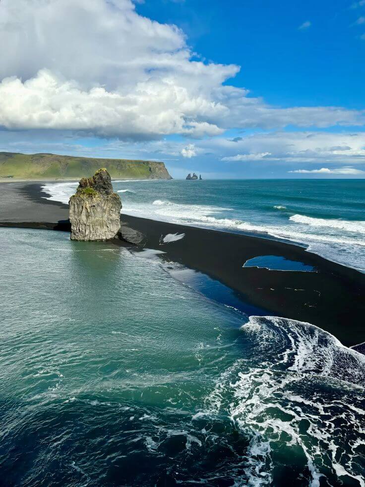 "Black sand beach in Iceland with dramatic rock formations, turquoise waves, and a clear blue sky."