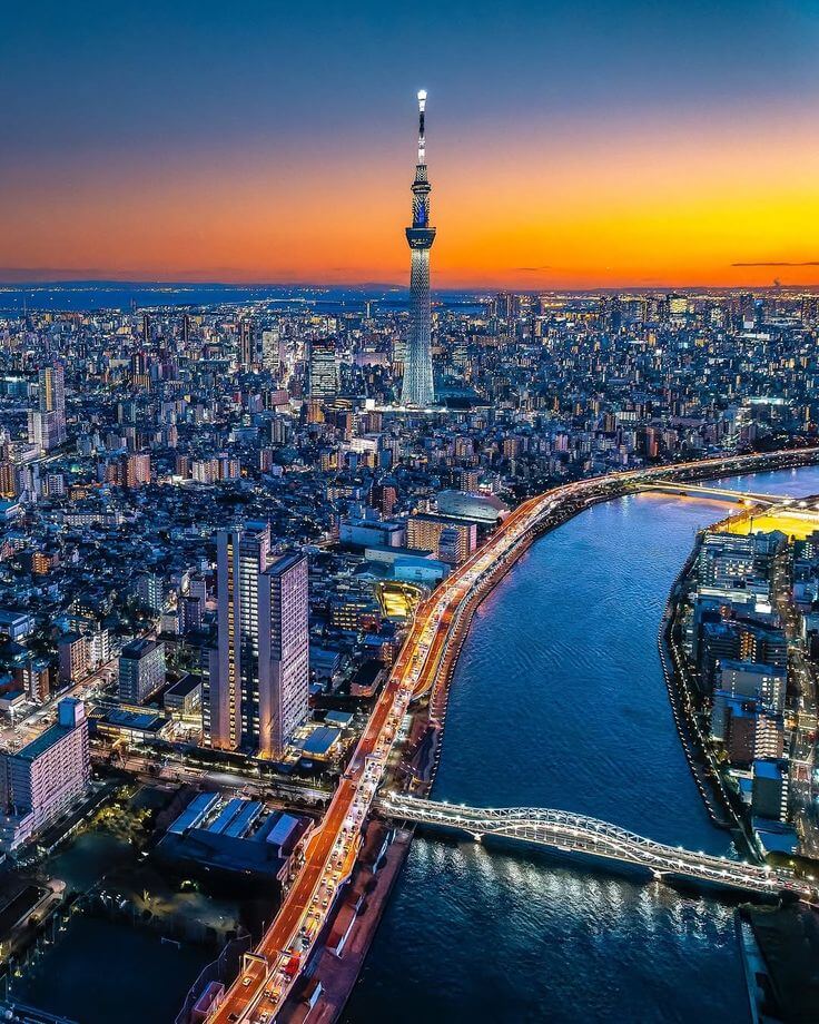 "Tokyo skyline at sunset with the Tokyo Skytree tower and illuminated city streets along the Sumida River."
