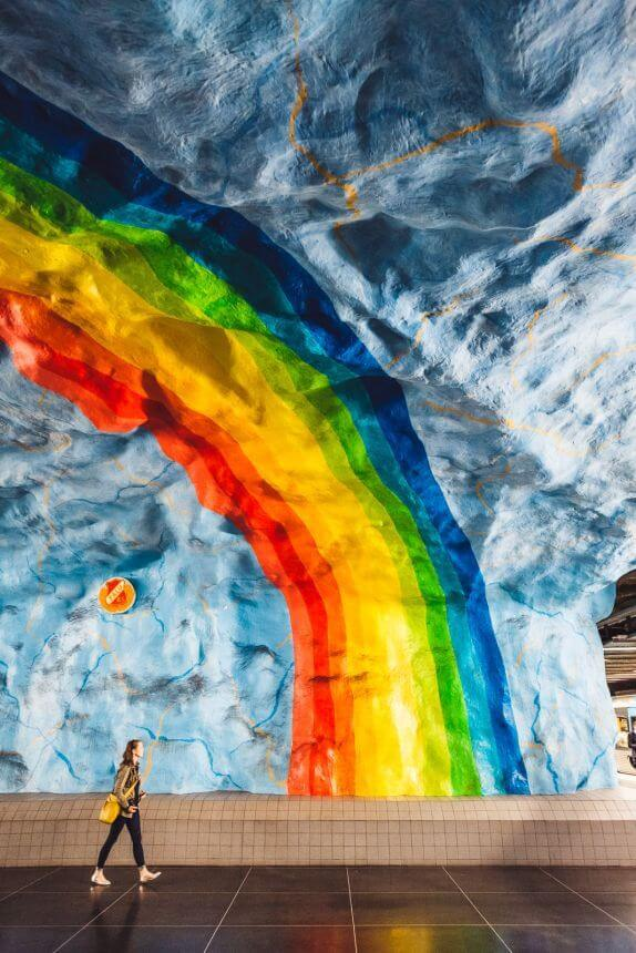 "Colorful rainbow mural in Stockholm's subway station with a woman walking by."