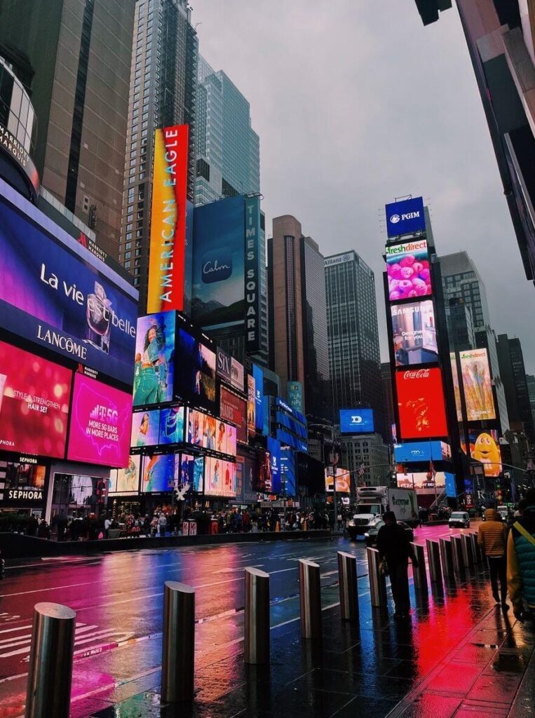 "Times Square in New York City with vibrant digital billboards and wet streets reflecting the colorful lights."
