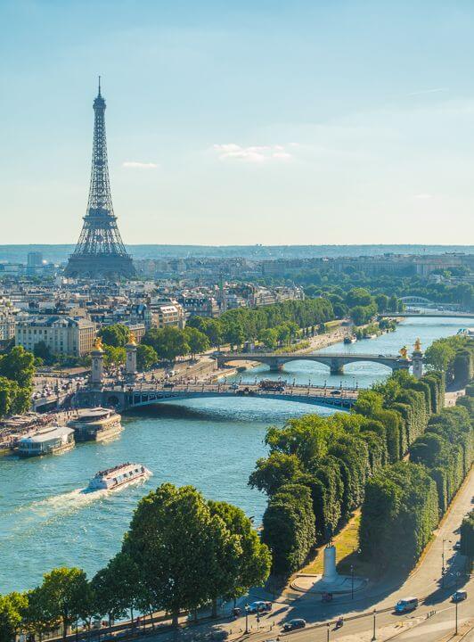 "Scenic view of the Eiffel Tower in Paris with the Seine River and tree-lined streets under a clear blue sky."