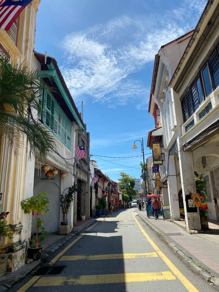 "Charming street in Penang, Malaysia, with colorful heritage buildings and a bright blue sky."