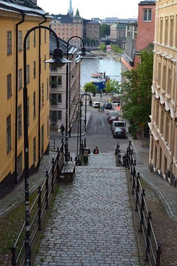 "View down a cobblestone street in Södermalm, Stockholm, with lamps and a glimpse of the waterfront."