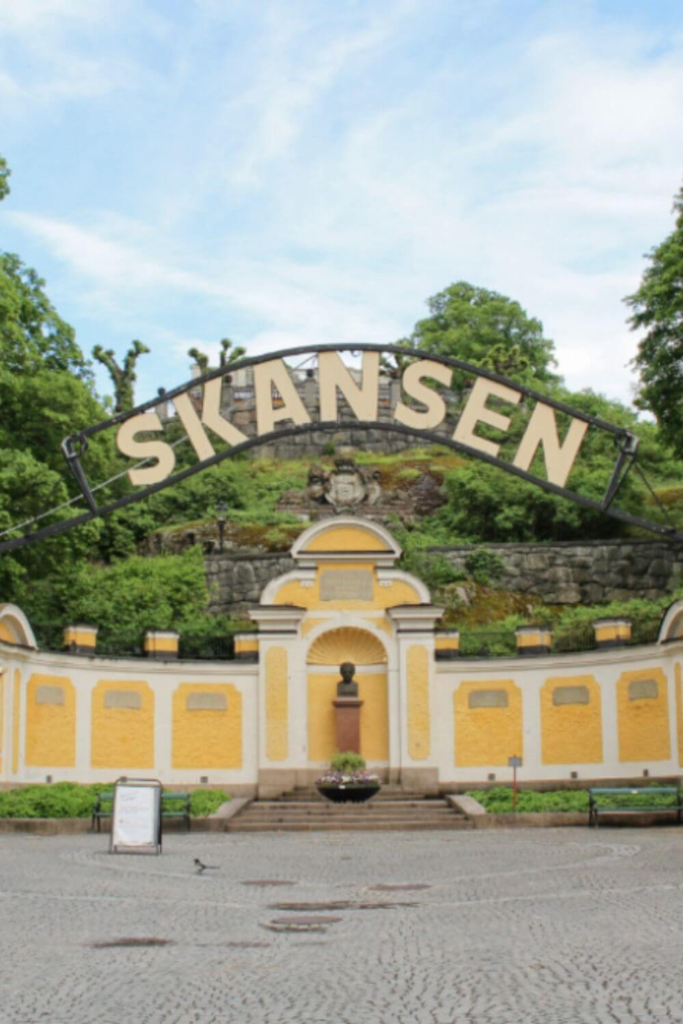 Entrance gate of Skansen open-air museum in Stockholm with yellow historic architecture and greenery.